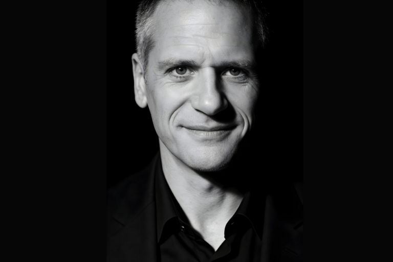 Close-up black-and-white portrait of a man with a gentle smile against a dark background.